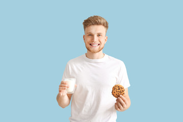 Handsome young man with tasty cookie and glass of milk on color background