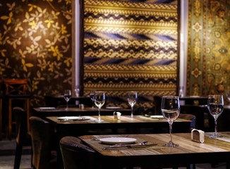 Empty wine glasses and tableware close up view on wooden table in restaurant with silk rugs on the wall