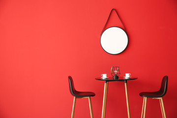 Table and chairs near color wall with mirror