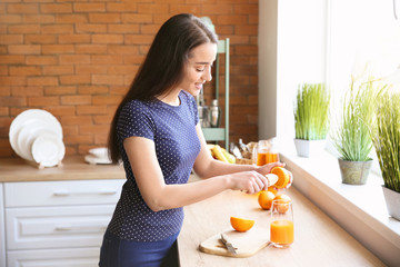 Beautiful woman preparing orange juice in kitchen at home