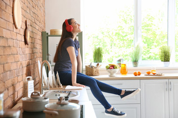 Beautiful woman listening to music in kitchen at home