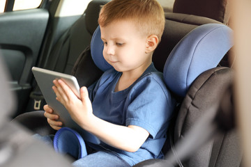 Little boy with tablet computer buckled in car seat