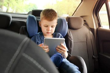 Little boy with tablet computer buckled in car seat