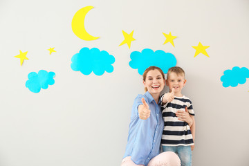 Cute little boy with nursery teacher showing thumb-up gesture on light background
