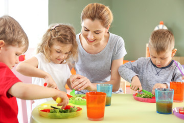 Nursery teacher with cute little children during lunch in kindergarten