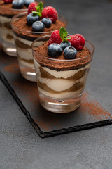 Classic tiramisu dessert with blueberries and raspberries in a glass on stone serving board on dark concrete background