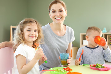 Obraz na płótnie Canvas Nursery teacher with cute little children during lunch in kindergarten