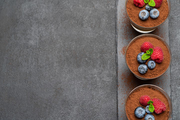 Classic tiramisu dessert with blueberries and raspberries in a glass on stone serving board on dark concrete background