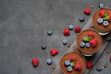 Classic tiramisu dessert with blueberries and raspberries in a glass on stone serving board on dark concrete background