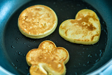 pancakes in the shape of a heart, flower and a circle on frying pan