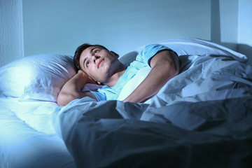Young man suffering from insomnia while lying in bed at night
