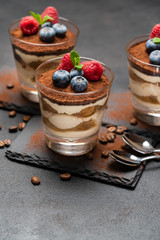 Classic tiramisu dessert with blueberries and raspberries in a glass on stone serving board on dark concrete background
