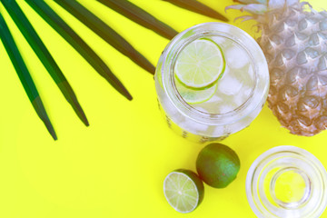 Cold fresh lemonade drink with lime slice and ice cubes in a jar on a yellow background