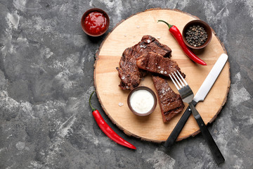 Board with tasty grilled meat on grey background