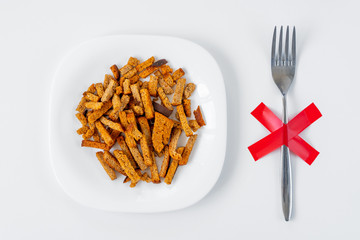 Crackers on white plate with fork with red X cross on the table. Dieting, unhealthy lifestyle concept