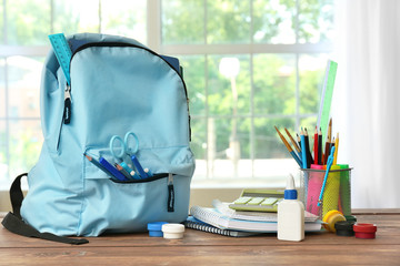 School backpack with stationery on table in room