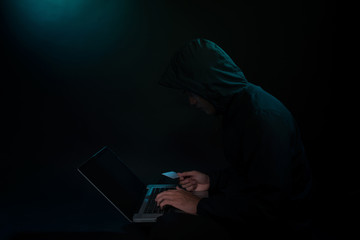 Internet Theft - a man holding a credit card while sat behind a laptop
