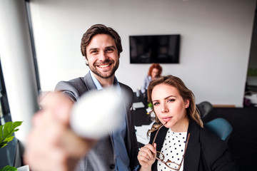 Two young business people in an office, looking at camera.