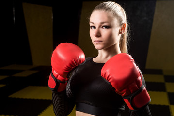 Pretty athletic woman in red boxing gloves posing in the gym