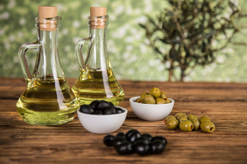 Olive oil, olive tree and green and black olives on a wooden table