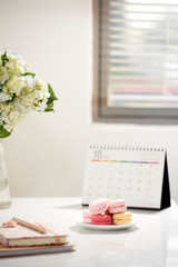 Office table desk. Feminine desk workspace frame with calendar, diary, hortensia bouquet and macaron on white background. ideas, notes or plan writing concept