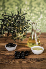 Olive oil and olive tree and black olives and bottles with olive on a wooden table