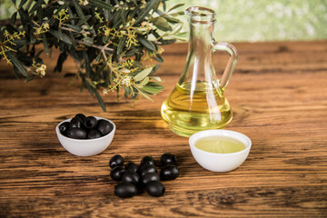 Olive oil and olive tree and black olives and bottles with olive on a wooden table