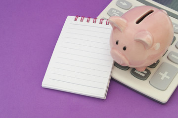 Piggy bank, calculator and blank notepad page for text message on purple background, concept for saving money and accounting