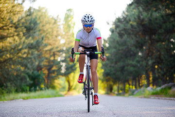 Fototapeta na wymiar Young Woman Cyclist Riding Road Bicycle on the Free Road in the Forest at Hot Summer Day. Healthy Lifestyle Concept.