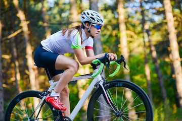 Plakat Young Woman Cyclist Riding Road Bicycle on the Free Road in the Forest at Hot Summer Day. Healthy Lifestyle Concept.