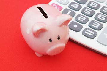 Piggy bank and calculator on red background close up