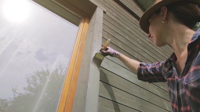 Woman worker painting wooden house exterior wall with paintbrush and wood protective color