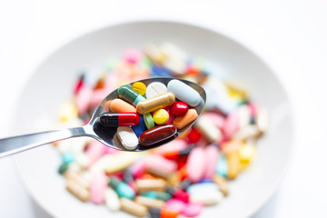 Various types of tablets, capsules and pills on  spoon with colorful medicine background.