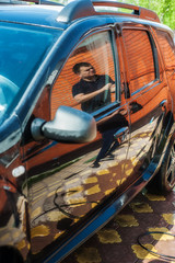 A man washes a black car from a hose with high-pressure water near the garage