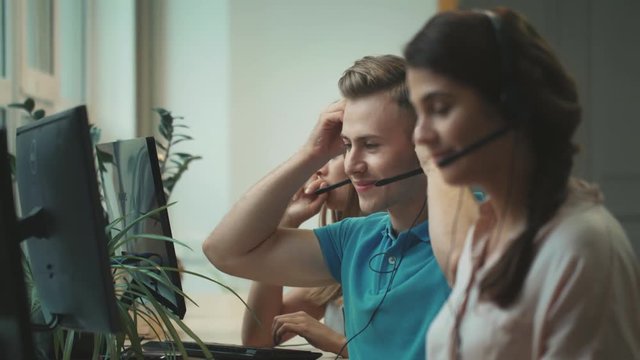 Young operator putting headset in call center. Smiling man talking with client