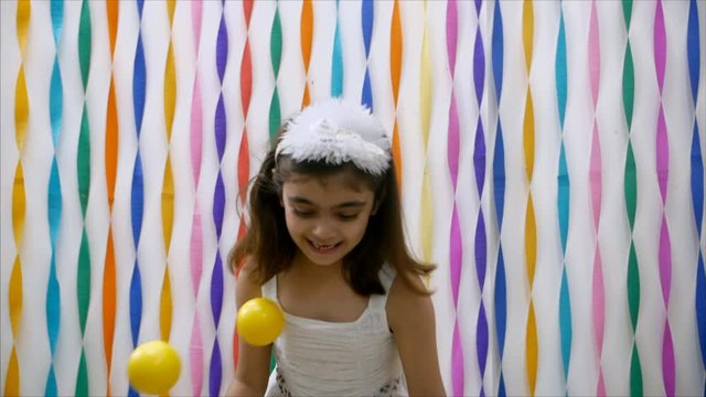 Excited little girl playing with smiley balls in front of the decorated wall. Indian school going girl in a white dress is playing with softballs at home