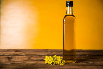 Rapeseed flowers and rapeseed oil in a bottle on the table - obrazy, fototapety, plakaty