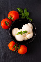 Food ingredient concept organic mozzarella cheese in black ceramic cup with  tomatoes and basil with copy space