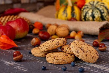 Chocolate cookies with chia seeds on old wooden table with autumn crops on blurred background.