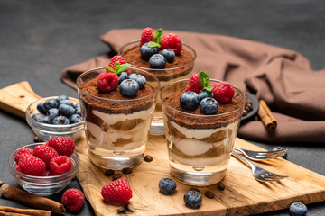 Classic tiramisu dessert with blueberries and raspberries in a glass on wooden cutting board on dark concrete background