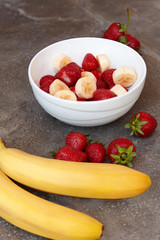 Healthy meal (breakfast), strawberry and bananas. Organic natural diet concept, white plate on wooden desk. Copy space.