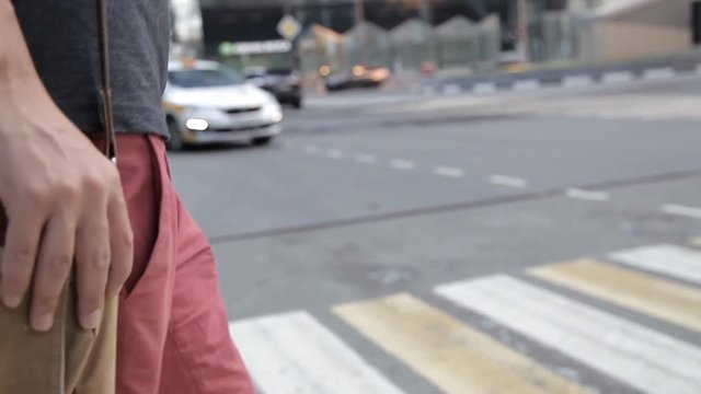 a man crosses the road at a pedestrian crossing, in the hands of a camera on his shoulder bag. On the background of a passing taxi. close-up of hands