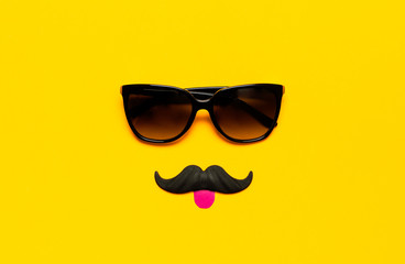 Creative party decoration concept. Black mustache, Sunglasses, props for photo booths, carnival parties on yellow background top view flat lay copy space. Father's day, Men's health awareness month