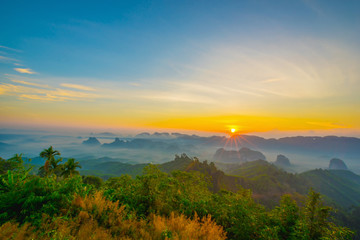 Beautiful mountain range with sky blue and orange light of the sun through the clouds in the sky, Background sky during Sunrise with fog on mountain, Abundant lush forest-Image