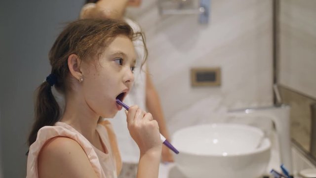 Two cute little sisters brush their teeth together as they get ready for bed. Close up shot.