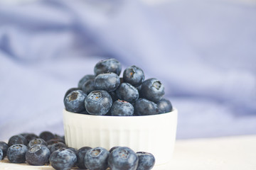 close up of bowl with blueberries on blue textile background