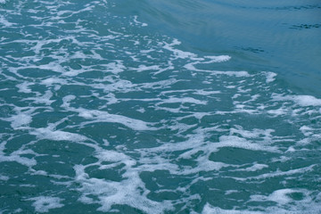Trail on the water from the boat, sea waves bubble foam from boat. Stock photo image of ocean waves and sea foam caused by the sail of a speed boat, water surface behind of fast moving motor boat