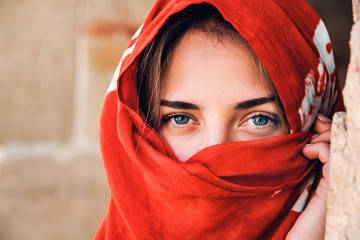 Portrait of an arabic young woman with her beautiful blue eyes in traditional islamic cloth red...