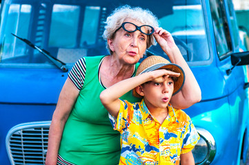 Trendy grandmothers with her grandson in beach colorful clothes near the retro car peer into the...