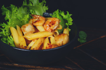 Pasta with fried scallops and lettuce in a dark plate